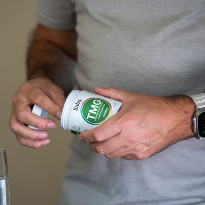 A man in a gray t-shirt opening a bottle of llabs. TMG (Betaine) Capsules as part of his daily routine.